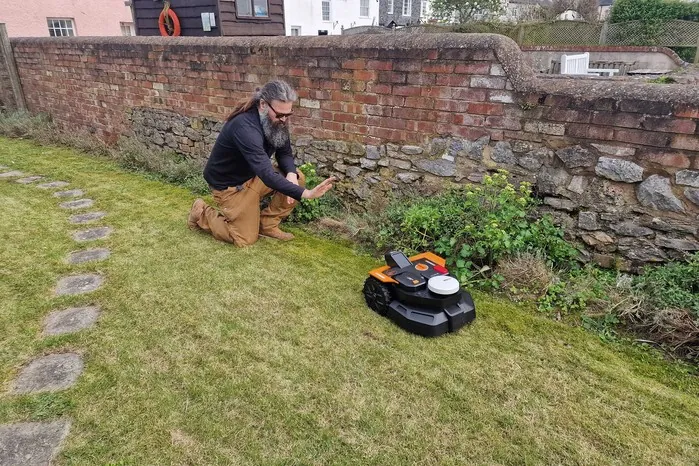 Rinsing a robotic mower deck clean beside a curved garden lawn